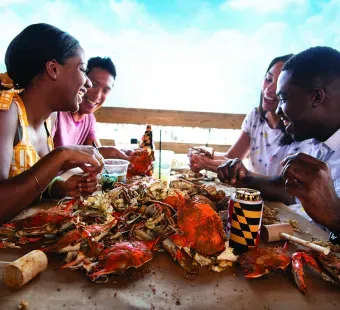 Four people smiling and enjoying their hot steamed Maryland crabs